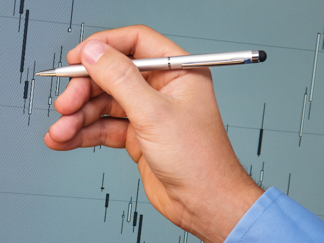Hand pointing at candlestick chart with a pen, analyzing potential market reversal points.
